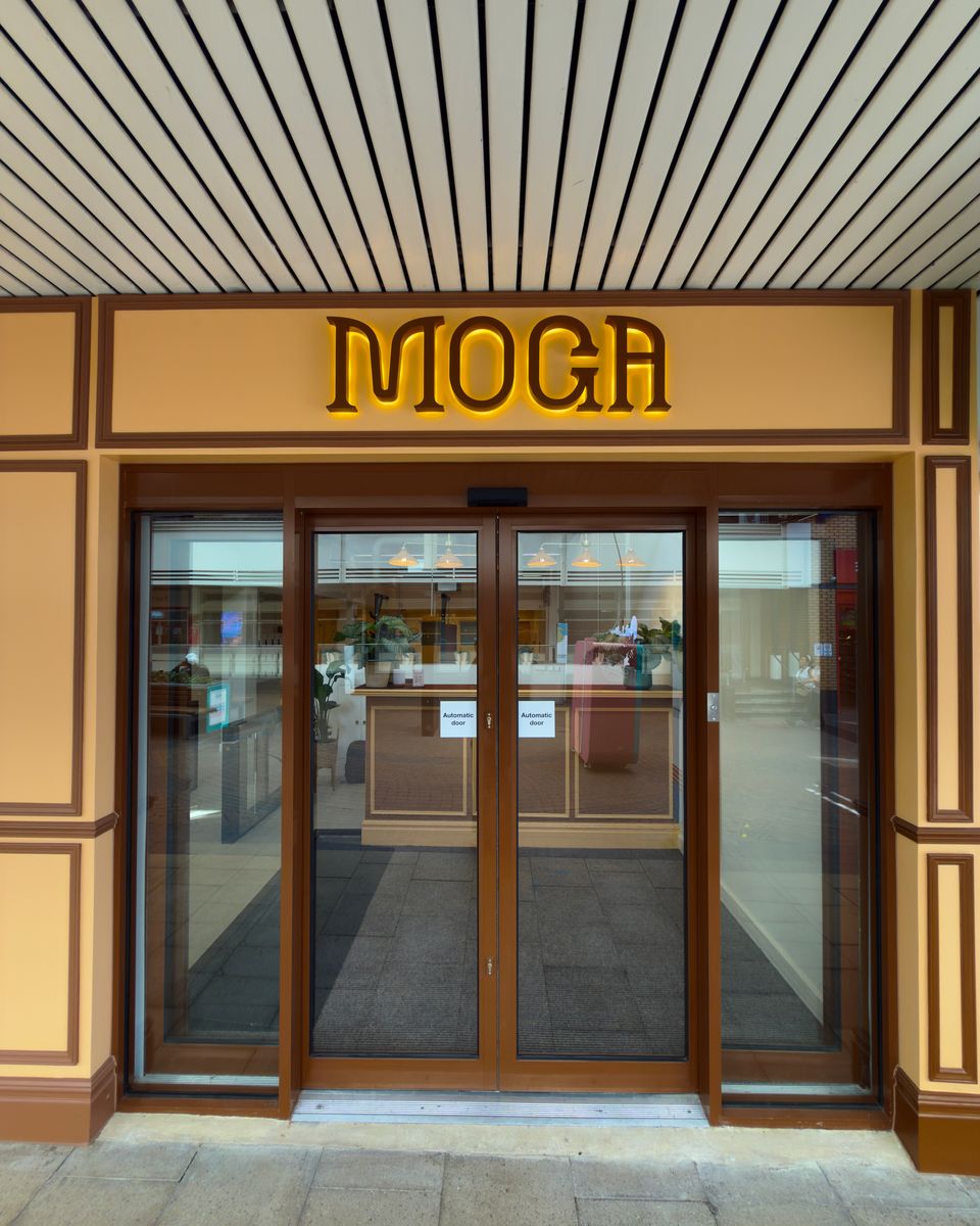 The MOGA entrance at 4–6 South Mall — an illuminated MOGA sign above wide automatic glass doors, under the shopping centre canopy